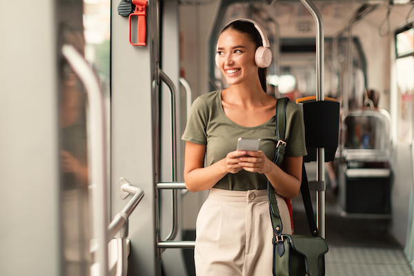 A commuter wearing headphones stands on the train and smiles.